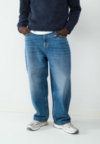 Niebieskie dżinsy o luźnym kroju, z przednimi kieszeniami, wyblakłą fakturą i średnim stanem. Połączone z jasnymi sneakersami.