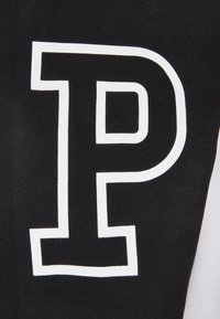 Lettre "P" en contour blanc imprimée sur tissu noir, affichant un contraste net et une typographie audacieuse.