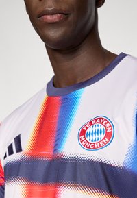 Φανέλα της FC Bayern München με κοντά μανίκια, με διαβαθμισμένο μοτίβο σε κόκκινο, μπλε και λευκό, και κυκλικό λογότυπο της ομάδας στο στήθος.