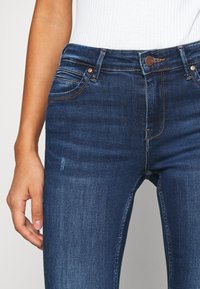 Mörkblå denimjeans med en figurnära design, femfickorsstil, koppardetaljer och subtila blekningar på framsidan.