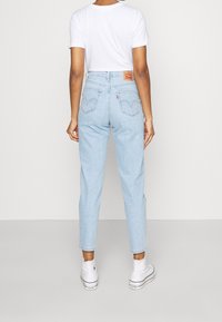 Ljust blå hög midja denimjeans med rak passform, bakfickor med sömnadsdetaljer, bärs med en vit t-shirt och vita sneakers.