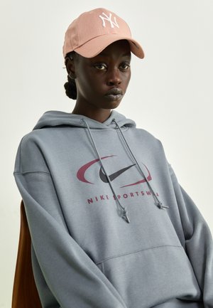 Szary hoodie z logo Nike w kolorze bordowym i czarnym. Połączony z jasnoróżową czapką z białym logo litery. Gładka tekstura.