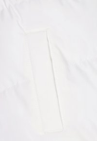 Weißer Stoff mit einer vertikalen, rechteckigen, eingenähten Taschenöffnung an einem Kleidungsstück, die Textur- und Nahtdetails zeigt.