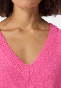 Roze gebreide trui met een diepe V-hals, voorzien van een gestructureerd patroon en geribbelde randen, gemaakt van een zachte en ademende stof.