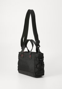 Sac fourre-tout noir en tissu durable, doté de poignées doubles, d'une bandoulière réglable, de détails élastiques sur les côtés et d'accents rouges à l'avant.