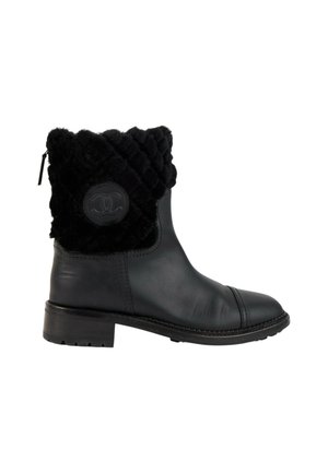 Bottine noire en cuir avec bordure matelassée en fourrure et patch rond avec logo sur le côté, petit talon bloc et fermeture éclair arrière.
