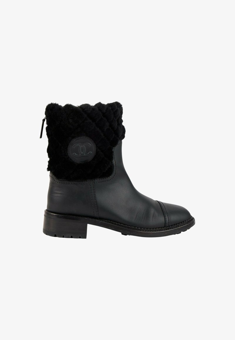 Bottine noire en cuir avec bordure matelassée en fourrure et patch rond avec logo sur le côté, petit talon bloc et fermeture éclair arrière.