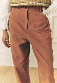 Roostevärvi ribidega velvetpüksid, millel on nööp-kinnis ja küljetaskud. Kandmisel mustrilise kudumiga kampsun.