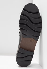 Semelle d'une chaussure noire avec des rainures courbes profondes pour l'adhérence, indiquant la taille 37 marquée près de la voûte.