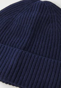 Marineblå ribbestrikket lue med brettet mansjett, som viser teksturerte ullfibre og vertikale sømmer.