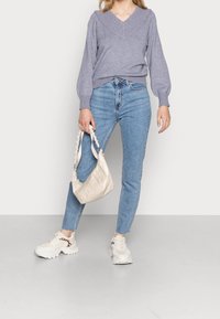 Suéter gris claro de pico, jeans azules de cintura alta, bolso beige con asas trenzadas y zapatillas blancas gruesas con detalles de estampado de leopardo.