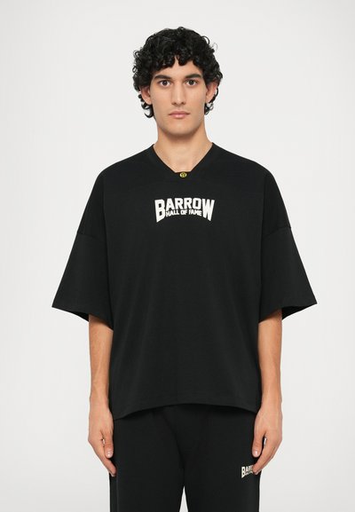 T-shirt nera oversize con maniche corte, con logo bianco "BARROW HALL OF FAME" sul petto. Tessuto morbido.