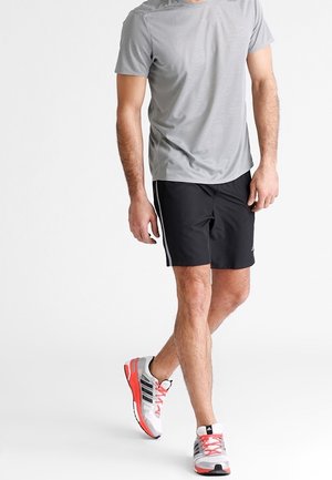 Herren-Sportbekleidung: kurzes graues T-Shirt und schwarze Shorts mit seitlichen Streifen. Sportliche Schuhe in Weiß, Schwarz und Rot. Entworfen für Bewegung und Komfort.
