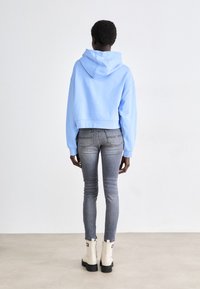 Croppad ljusblå hoodie med dragsnodd i huvan, i kombination med åtsittande grå jeans och vita ankelstövlar med svarta sulor.