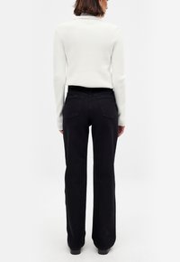 Jeans anchos negros con un acabado texturizado y dos bolsillos traseros, combinados con un suéter blanco ceñido de canalé. Ambos artículos son minimalistas.