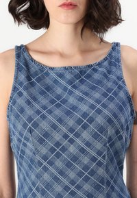 Denim obleka z kvadratnim izrezom, modrim karirastim vzorcem in brezrokavnim dizajnom s vidnimi šivi. Gladka tekstura.