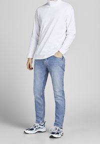 Vit långärmad turtleneck, ljusblå jeans och flerfärgade sportskor med vita, marinblå och teal accenter. Avslappnad passform.