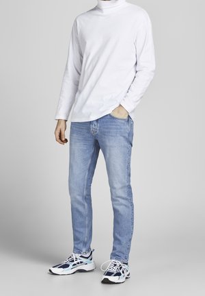 Jersey blanco de manga larga y cuello alto, vaqueros azul claro y zapatillas deportivas multicolores con acentos en blanco, azul marino y verde azulado. Ajuste casual.