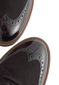 Černé semišové a lesklé lakované kožené brogues boty s designem wingtip, dekorativními perforacemi a hnědou gumovou podrážkou.