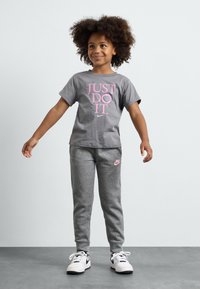 Pilkas trumpas rankovėmis marškinėliai su rožiniu užrašu "TIESIOG DARYK TAI." derinami su pilkomis treningo kelnėmis, ant kurių yra rožinė Nike logotipas, vilkima su baltais sportbačiais.