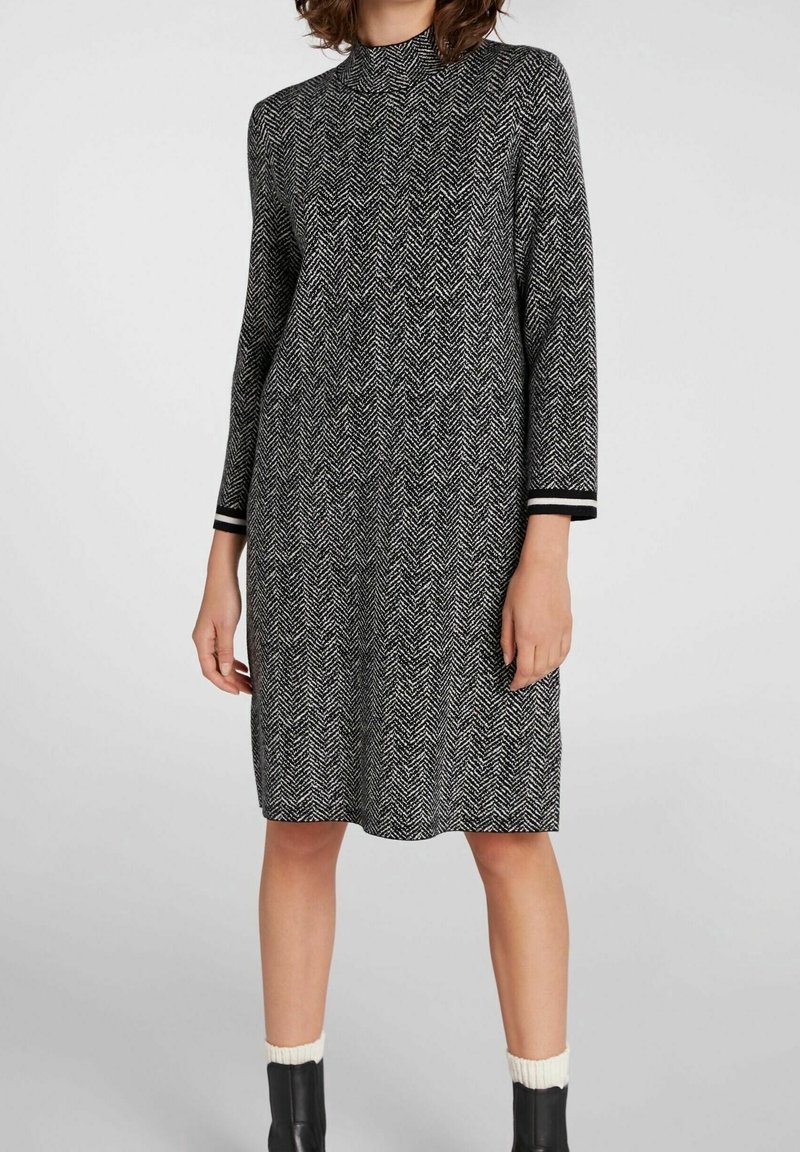 Robe à motif en chevrons noir et blanc. Col haut, manches longues et poignets rayés contrastants. Mi-longue avec une coupe décontractée.