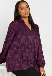 Blusa viola con motivo floreale, scollatura a V, maniche lunghe a sbuffo, tessuto testurizzato e dettagli con bottoni lungo il davanti.