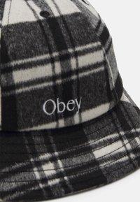 Pălărie tip bucket în carouri alb-negru, realizată dintr-un material moale, având pe față un logo distinct brodat "Obey".