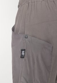 Gray lightweight shorts with textured fabric, featuring a large side pocket, a snap button closure, and a black fabric label on the pocket.