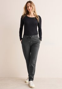 Haut noir à manches longues associé à un pantalon de survêtement gris avec taille à cordon, poches latérales et baskets blanches. Tissu lisse et design ajusté.