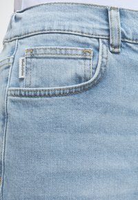 Φωτογραφία κοντινού πλάνου σε ανοιχτό μπλε τζιν παντελόνι που δείχνει μικρή τσέπη με ετικέτα μάρκας "Modström" και εμφανείς λεπτομέρειες ραφής.