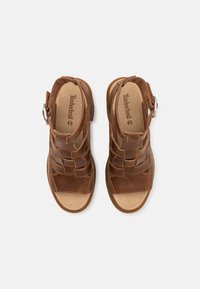 Brune skinnsandaler med vevd design, spenne og flat såle. Fotbehandlingen har en myk tekstur og preget merkevarelogo.