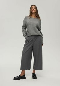Szary sweter dzianinowy z okrągłym dekoltem, zestawiony z szerokimi szarymi spodniami. Czarne błyszczące buty dopełniają outfit. Gładkie faktury w całym zestawieniu.