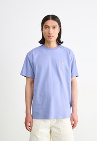 Purple cotton t-shirt with short sleeves, round neck, featuring a small yellow logo on the chest, worn with light-colored pants.