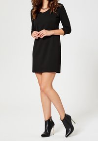 Svart knälång klänning med trekvartslånga ärmar och V-ringning, i kombination med svarta högklackade ankelstövlar med gulddragkedjor.