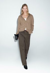 Light brown cardigan, white top, dark brown pants, and black clutch. Features relaxed fit, long sleeves, and subtle texture details.