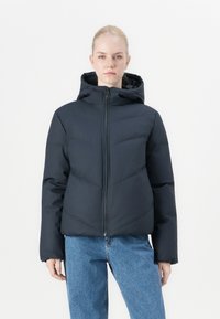 Puffer jacket in dark navy, featuring a hood, front zipper, and contrasting quilted pattern. Worn with light blue jeans.