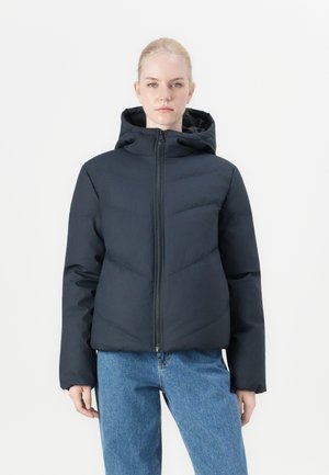 Dunjakke i mørk marine, med hette, glidelås foran og kontrasterende quiltet mønster. Iført med lyseblå jeans.