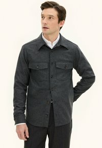 Dark gray, wool-blend jacket with a button-up front, a pointed collar, and two chest pockets. Features a straight hem and buttoned cuffs.