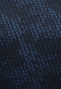 Σκούρο μπλε ύφασμα με επαναλαμβανόμενα, ελαφρώς παραμορφωμένα γράμματα που σχηματίζουν τη λέξη "LAGERFELD" σε μοτίβο δικτύου.