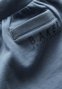 Modrá bavlněná tkanina s texturovaným povrchem, obsahující přišit pocket a černý potisk "BAKER by TED BAKER" na materiálu.