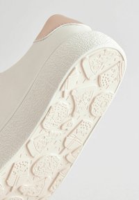 Baskets blanches avec une semelle texturée, présentant un accent de talon rose. La semelle comporte des motifs en relief ressemblant à des aliments.