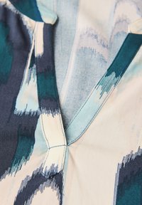 Close-up of a fabric featuring a colorful, abstract pattern with navy, teal, and light shades, emphasizing texture and design details.