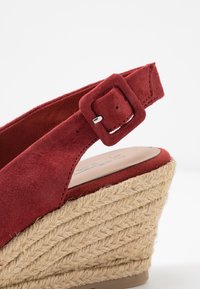 Rode suede wedge sandaal met een getextureerd jute platform en band, voorzien van een vierkante gesp sluiting bij de enkel.