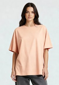 Persiko spalvos per didelis T-puloveris iš minkštos medvilnės, su apvaliu iškirpimu, žemai nukaramomis petnešomis ir trumpomis rankovėmis, su lygiu paviršiumi.