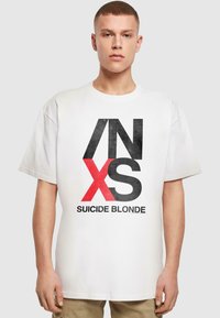 Hvid bomulds t-shirt med stort grafisk print i sort og rødt, med teksten "INXS SUICIDE BLONDE." Korte ærmer og afslappet pasform.