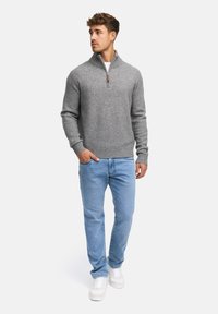 Grå zip-tröja i mjukt tyg, tillsammans med ljusblå jeans och vita sneakers. Tröjan har ribbade ärmslut och fåll.