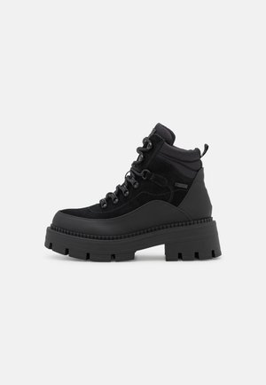 Bottines à plateforme noires et épaisses avec un laçage à l'avant, un col rembourré et une semelle robuste, présentées sur fond blanc uni.