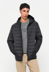 Schwarze gepolsterte Jacke mit Kapuze, Reißverschluss und strukturiertem Paneldesign. Getragen über einem grauen Sweatshirt mit Drucktext. Lässige Passform.