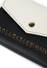 Svart och vit texturerad läderplånbok med tryckknappsstängning, som har guldtonad branding på den svarta delen och kontrastsöm.