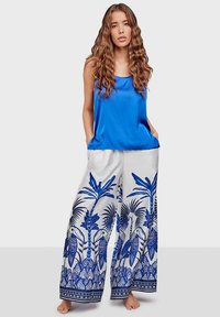 Blue satin top with thin straps paired with white wide-leg pants featuring blue tropical print, including palm trees and parrots.